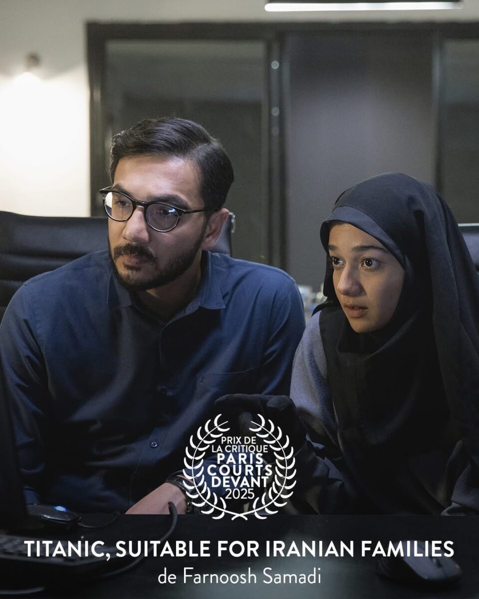 L'immagine raffigura una scena dal film 'Titanic, Suitable for Iranian Families' di Farnoosh Samadi. Un uomo con la barba, occhiali e camicia blu siede accanto a una giovane donna con hijab nero, entrambi con espressioni serie mentre guardano uno schermo.